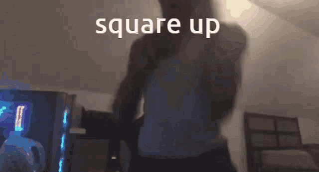 a man in a white tank top is standing in a dark room with the words square up written above him