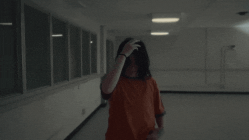 a woman in an orange shirt stands in a dark hallway