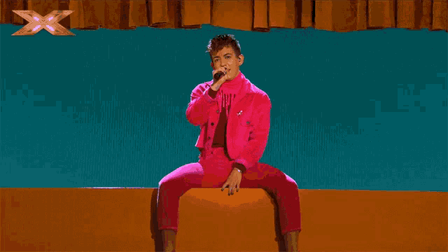 a man in a pink suit is singing into a microphone on a stage