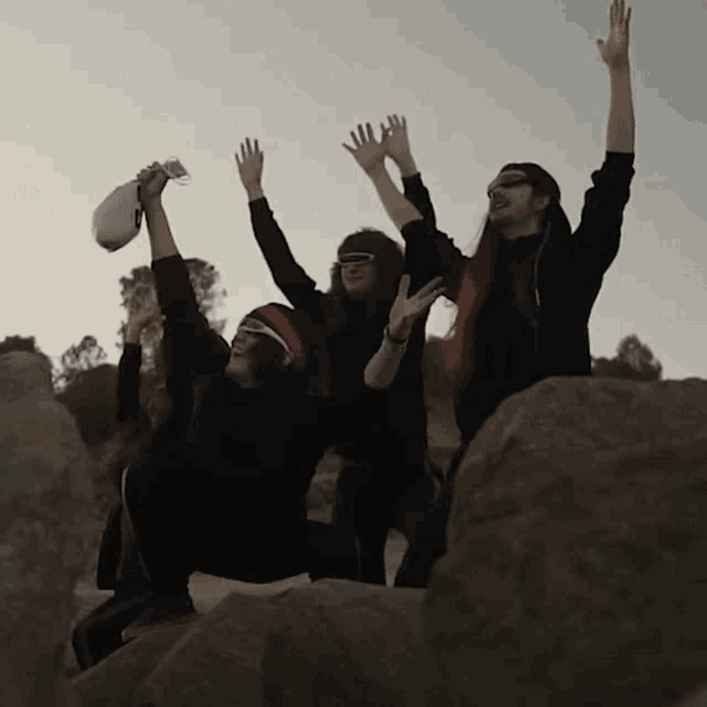 a group of people are sitting on rocks with their hands in the air