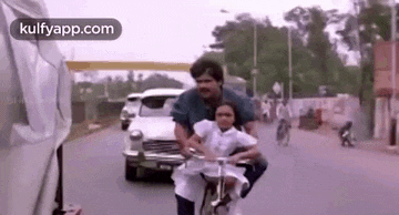 a man is riding a bicycle with a little girl on his back on a street .