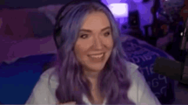 a woman with purple hair is wearing headphones and smiling while sitting in front of a computer screen .