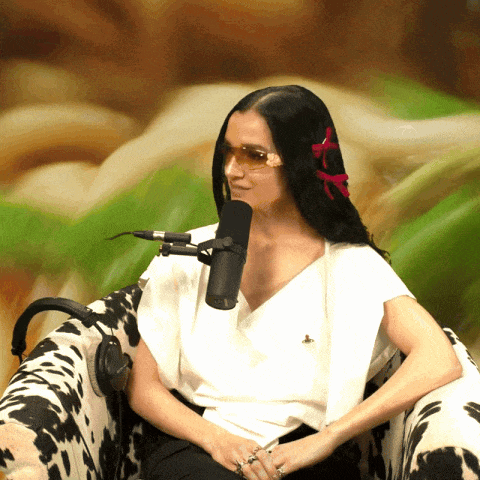 a woman wearing sunglasses sits in front of a microphone in a chair