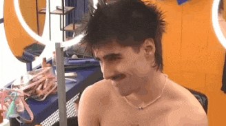 a shirtless man with a mustache and a necklace is sitting in front of a mirror .