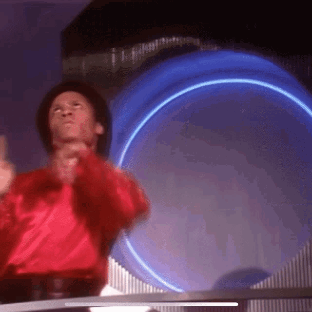 a man in a red shirt is dancing in front of a blue circle