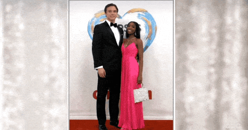 a man in a tuxedo and a woman in a pink dress pose for a picture on a red carpet