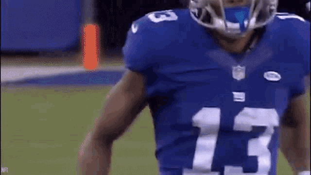 a football player wearing a blue jersey with the number 13 on it is standing on a field .