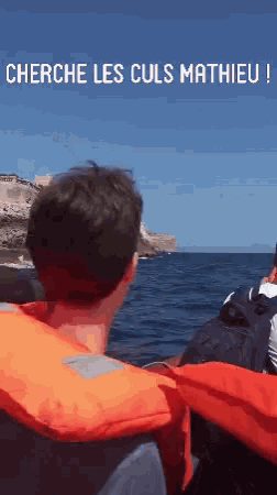 a man wearing an orange life jacket looks out over the ocean with the words cherche les culs mathieu above him