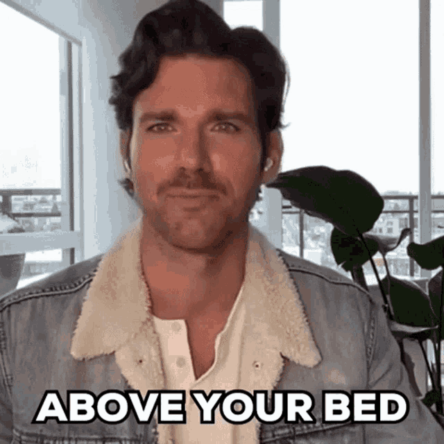 a man in a denim jacket with the words above your bed below him