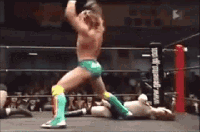two men are wrestling in a wrestling ring and one of them is wearing green shorts and yellow knee pads .