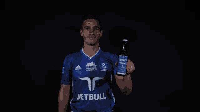 a man in a jetbull jersey holds up a bottle of beer