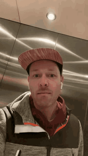 a man wearing a hat and ear buds is standing in an elevator