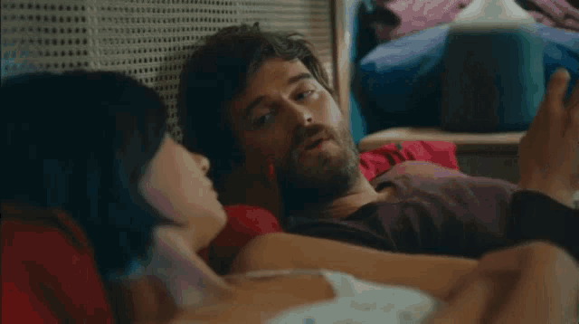 a man and a woman are laying on a bed and the man is using a cell phone .