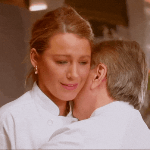 a man kisses a woman on the cheek while wearing a chef 's coat