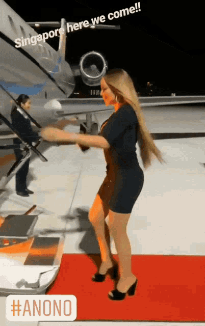 a woman standing on a red carpet in front of an airplane with singapore here we come written on it