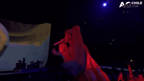 a woman in a red top is singing into a microphone in front of a screen that says agchile.com