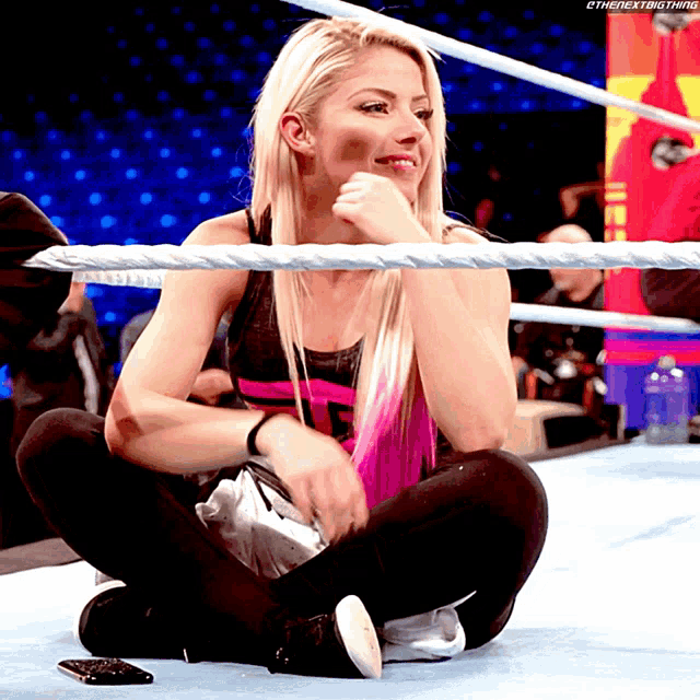 a woman sits on the floor in a wrestling ring with the nextbigthing written on the bottom right