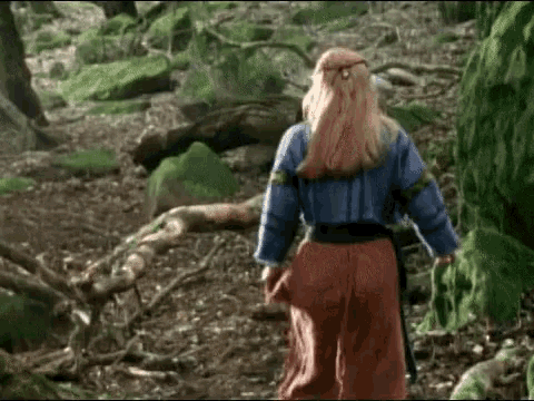 a woman in a blue top and red skirt is walking through a forest