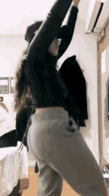 a woman in a black crop top and grey sweatpants is dancing in a bedroom .