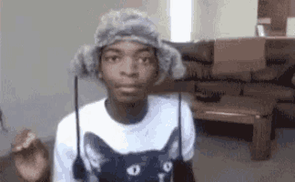 a young man wearing a furry hat and a cat shirt is standing in a living room .