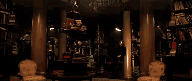 a man is standing in a dark room with a lot of books and candles .