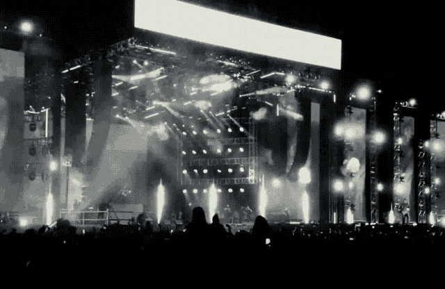 a crowd of people watching a concert with a large screen behind them that says ' a '