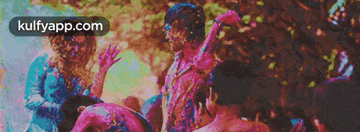 a group of people are playing with colored powder and the website kulfyapp.com is visible