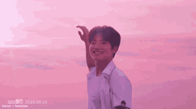a young man in a white shirt is standing on a pink beach with his hand in the air .