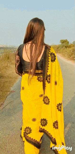 a woman in a yellow saree is walking down a dirt road
