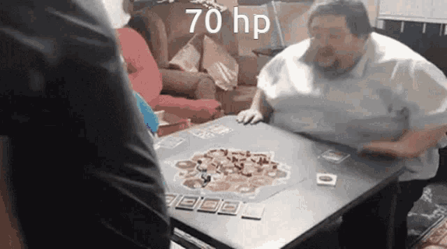 a fat man is sitting at a table playing a board game with cards .