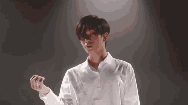 a young man in a white shirt is standing in front of a dark background and holding something in his hand .