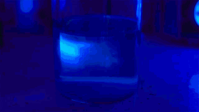 a glass filled with glow in the dark liquid is glowing in the dark .