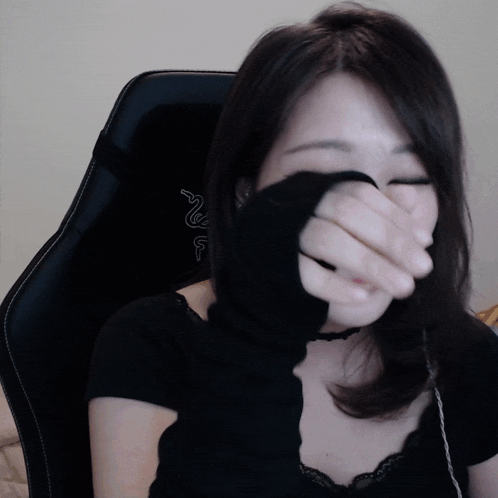 a woman covering her face with her hand while sitting in a chair with a razer logo on it