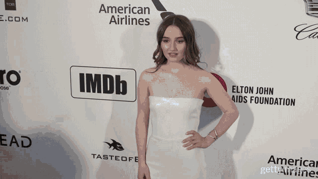 a woman in a white dress stands on a red carpet sponsored by american airlines
