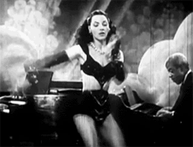 a woman is dancing in a black and white photo while a man plays a piano .