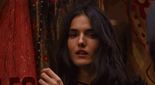 a woman with long dark hair is standing in front of a curtain with a s on it