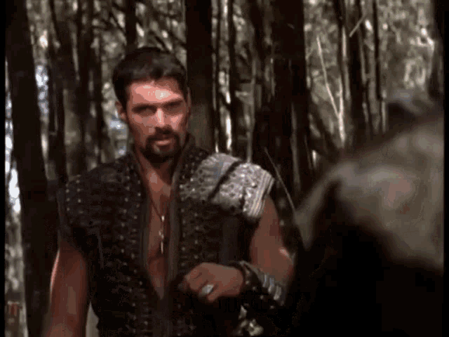 a man with a beard is standing in the woods holding a hammer .