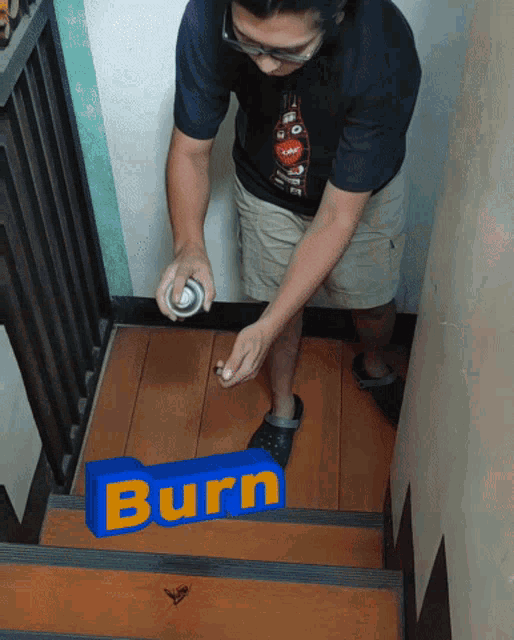 a man spray paints a blue sign that says burn on a set of stairs