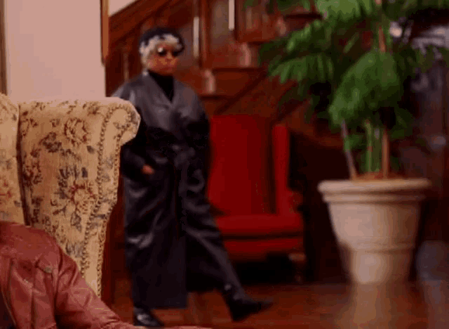 a woman in a black coat and sunglasses is standing in front of a staircase
