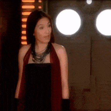 a woman in a black dress and red scarf is standing in a dark room with three lights behind her .