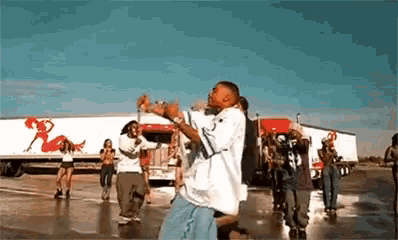 a group of people are dancing in a parking lot in front of a semi truck .
