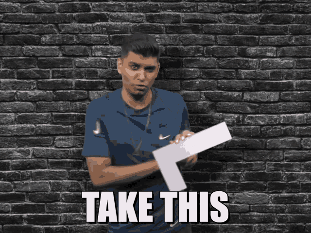 a man holding a piece of paper in front of a brick wall with the words take this above him