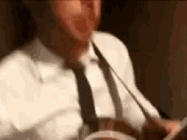a man in a white shirt and tie is sitting at a table with a plate of food .