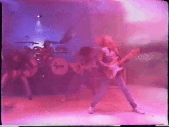 a man playing a guitar in front of a drum set with the letter t on it