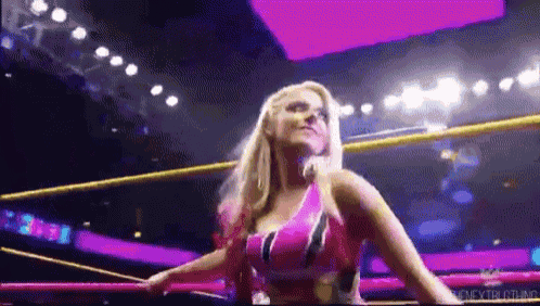 a woman is standing in a wrestling ring wearing a pink top and a purple top .