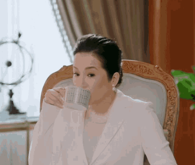 a woman in a white suit is drinking from a silver cup