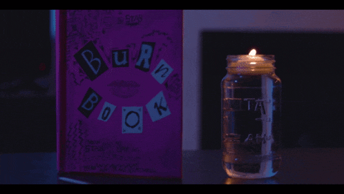 a burn book sits next to a mason jar with a candle in it