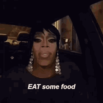 a drag queen is sitting in a car and says eat some food