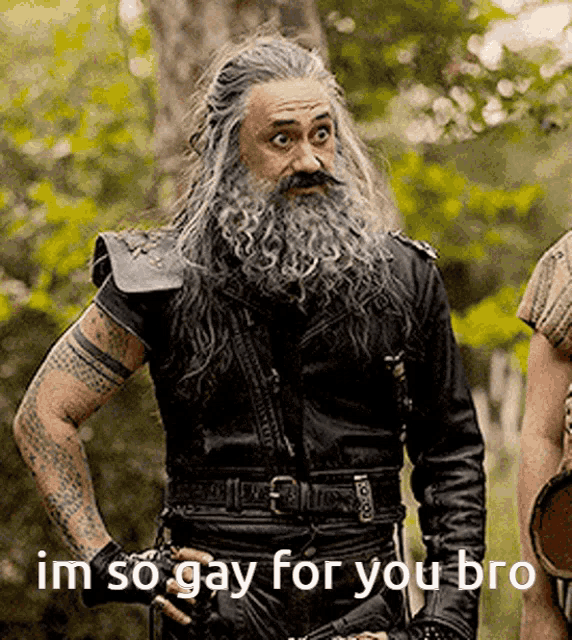 a man with a beard and long hair is standing in the woods and says im so gay for you bro