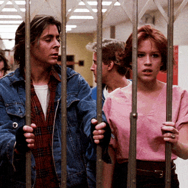 a man in a denim jacket and a woman in a pink shirt are behind a fence